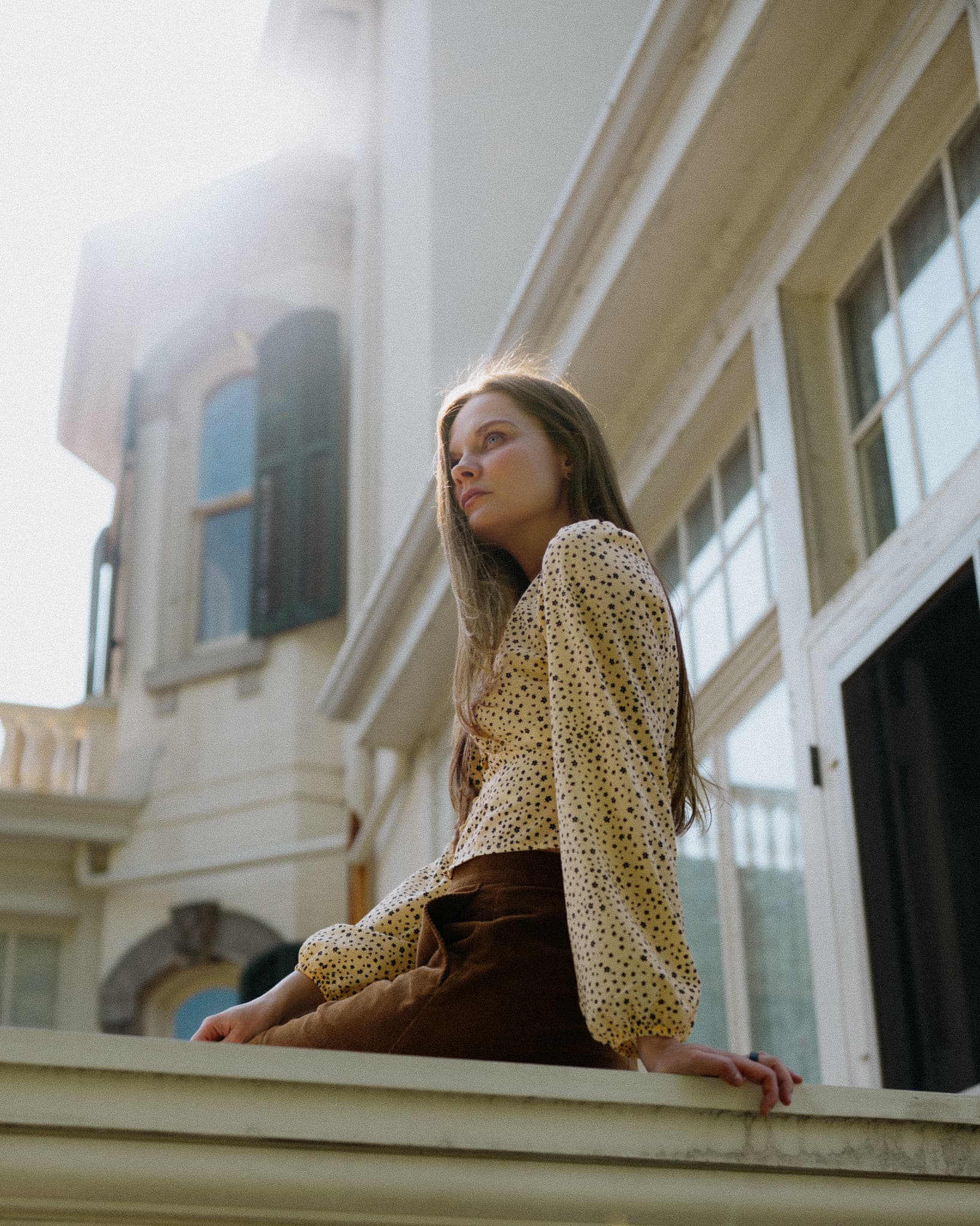 Girl sitting on a ledge beside a sunlit classical building