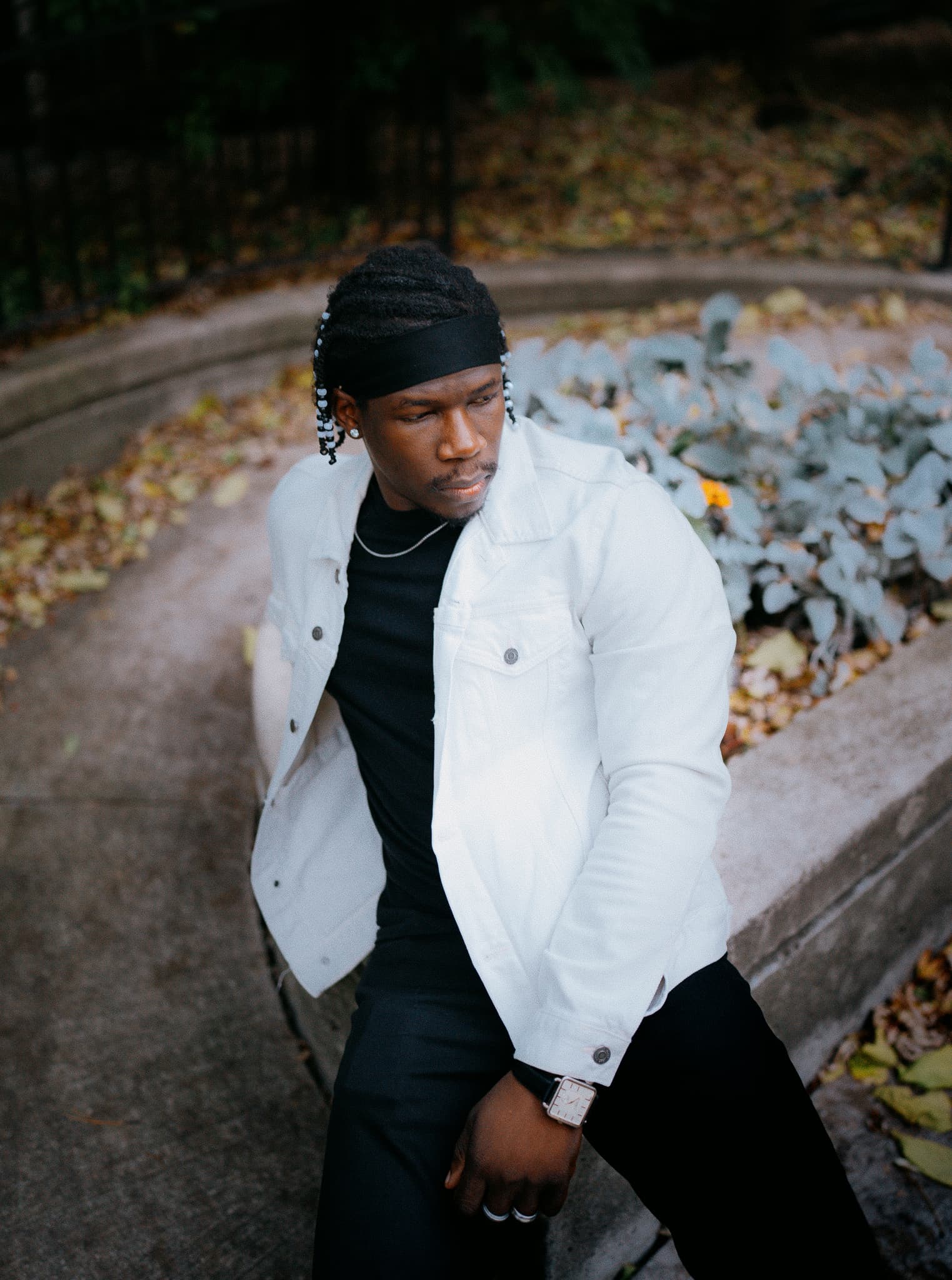 Man in a white jacket leaning on a stone planter among autumn leaves